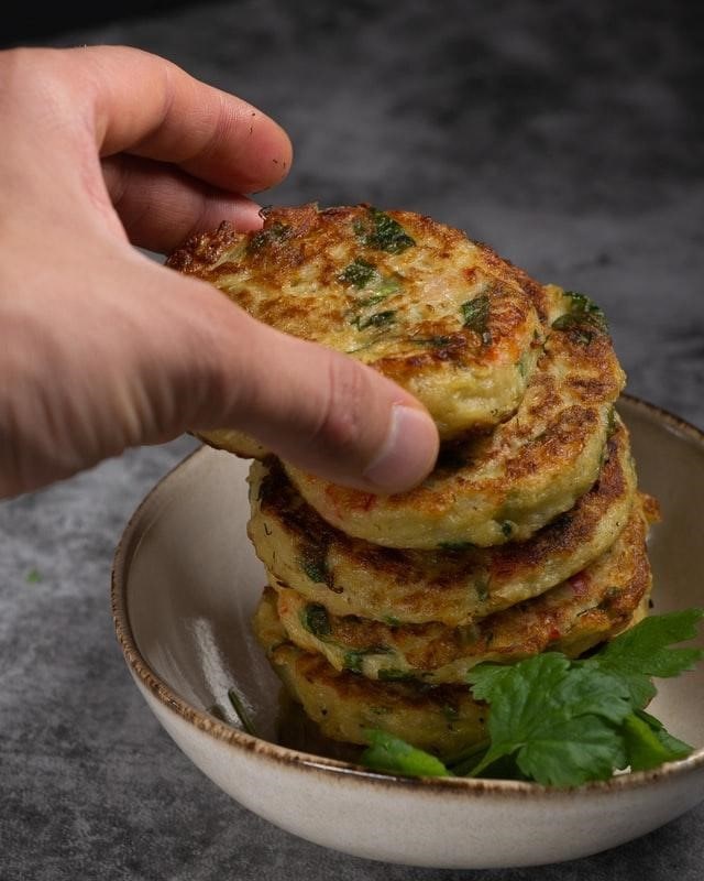 An individual taking a potato pancake from a plate